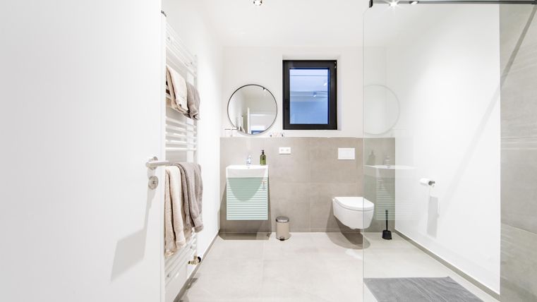 Ein modernes Badezimmer mit hellen Wänden und einer klaren Duschabtrennung. Es gibt einen Waschbecken, eine Toilette und einen Handtuchhalter.