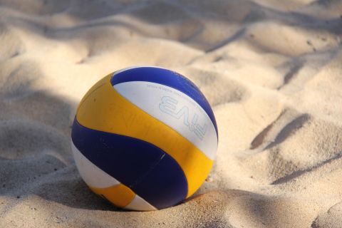 A blue, yellow, and white striped volleyball lies on a sandy surface.