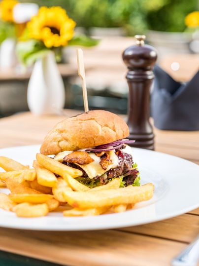 A juicy burger with lettuce, cheese, and a slice of bacon. Served with crispy fries on a white plate.
