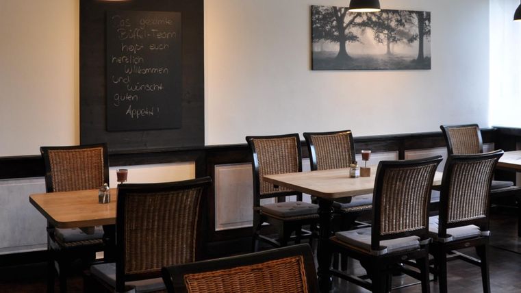 A cozy restaurant with wooden chairs and tables. On the wall hangs a board with writing and a picture of trees.