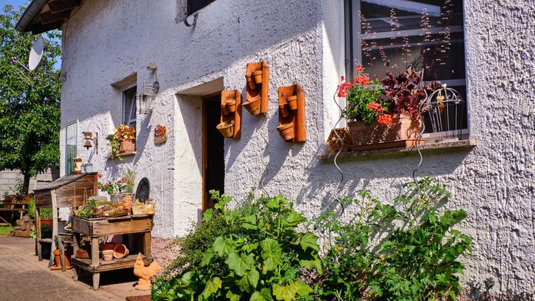 Ein charmantes Haus mit weißer Fassade und dekorativen Blumentöpfen. Der Garten ist grün und einladend, mit einem kleinen Holztisch und Pflanzen.