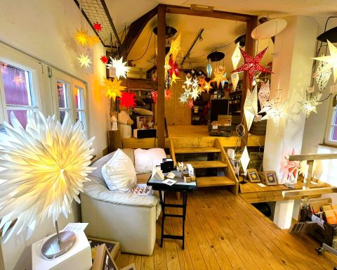 A cozy room with a wooden floor that displays festive lights and decorations. In the foreground, there is a comfortable couch and a table with various items.