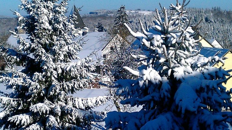Ein verschneites Winterland mit schneebedeckten Tannen und Dächern. Die Sonne scheint auf die friedliche Landschaft.