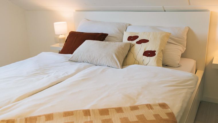 Een gezellige slaapkamer met een groot bed en meerdere kussens. Zacht licht van een nachtlampje creëert een uitnodigende sfeer.