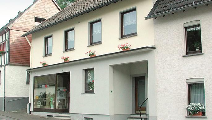 A two-story building with white walls and several windows. In the front, there is a store with a large entrance door.