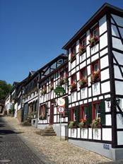 A picturesque half-timbered house on a quiet street. The facade is adorned with flowers and the sky is clear and blue.