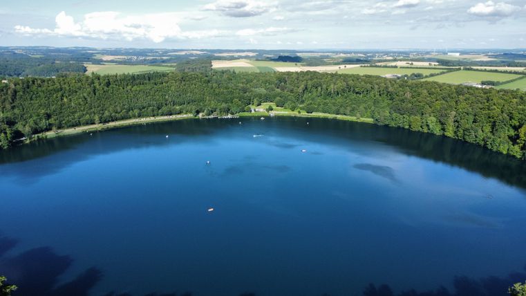 Een rustige meer omringd door groene bossen en weilanden. Het wateroppervlak weerspiegelt de heldere lucht.