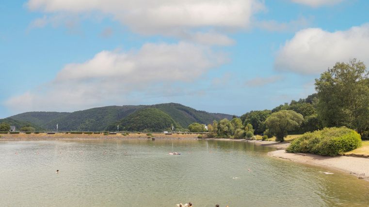 A peaceful bay with clear water and gentle waves. In the background, hills and green trees can be seen.