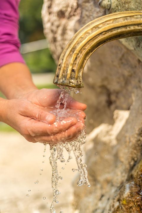 Hände fangen Wasser aus einem antiken, goldfarbenen Brunnen im Kurpark auf. Das Wasser sprudelt klar und erfrischend.