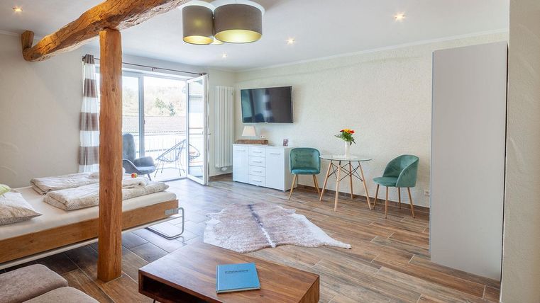 Ein modernes Zimmer mit Holzdetails, einem großen Fenster und Zugang zum Balkon. Es gibt ein Doppelbett, einen Tisch und Stühle sowie eine gemütliche Atmosphäre.