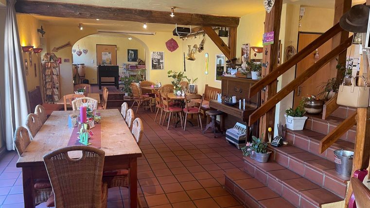 Ein einladendes Café mit Holztischen und Stühlen. Die Wände sind in warmen Farben gestrichen und Pflanzen sorgen für eine gemütliche Atmosphäre.