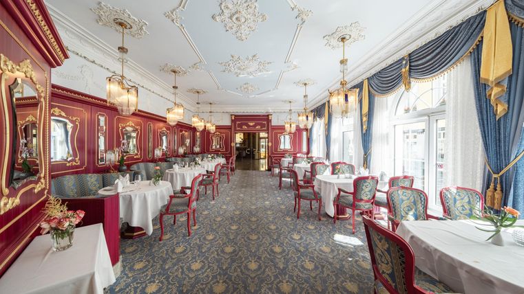 Een elegante eetzaal met rode muren en stijlvolle meubels. Grote ramen laten veel licht binnen en zorgen voor een uitnodigende sfeer.