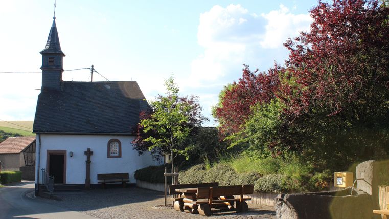 A small church with a slender tower stands on a quiet street. Surrounded by trees and green space, the place radiates a peaceful atmosphere.