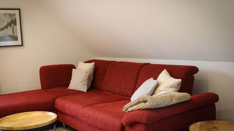 A cozy red sofa with cushions, next to small wooden tables. The room has a simple and inviting atmosphere.