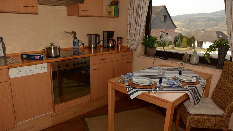 A bright kitchen with wooden cabinets and modern appliances. A set table stands next to a window with a beautiful view.