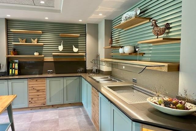Eine moderne Küche mit hellgrünen Wänden und Holzregalen. Die Arbeitsfläche ist ordentlich und mit verschiedenen dekorativen Elementen geschmückt.