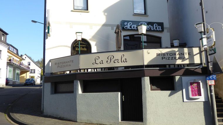Ein Restaurant mit dem Namen "La Perla" an einer Straßenecke. Die Fassade zeigt eine moderne Gestaltung mit einem einladenden Außenbereich.
