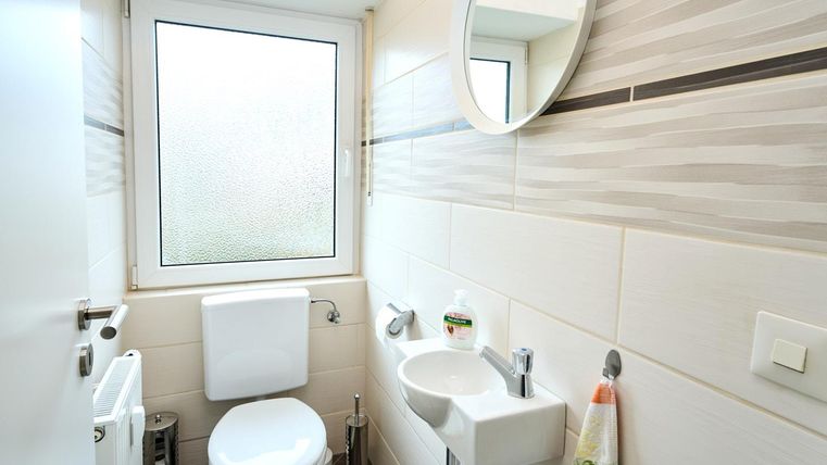 Ein modernes Badezimmer mit einem WC, Waschbecken und einem spiegel. Das Fenster lässt viel Tageslicht herein.