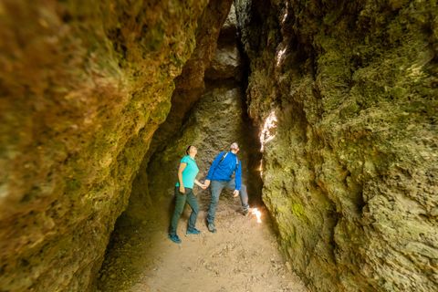 Ein Paar steht in einer engen Höhle und schaut gebannt nach oben. Die Wände sind aus grauem Fels, und das Licht scheint durch einen Spalt.