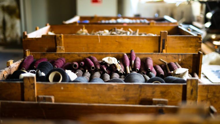 Wooden boxes with various spools of thread in a workshop. The threads are in different colors and sizes.