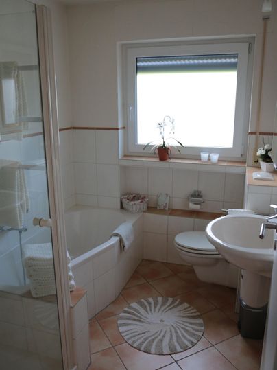 Ein helles Badezimmer mit einer Badewanne, Dusche und einem Waschbecken. Pflanzen und dekorative Elemente verleihen dem Raum eine einladende Atmosphäre.