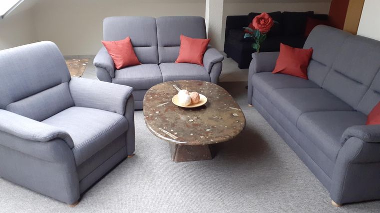 Een moderne woonkamer met twee grijze banken en een salontafel. Op de tafel liggen enkele broodjes en een plant siert de ruimte.