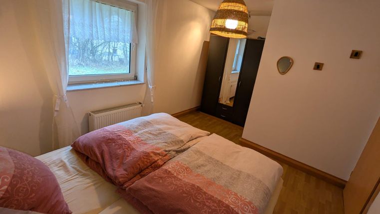 A cozy bedroom with two beds and soft, colorful blankets. The room has a window with curtains and warm lighting from a beautiful lamp.