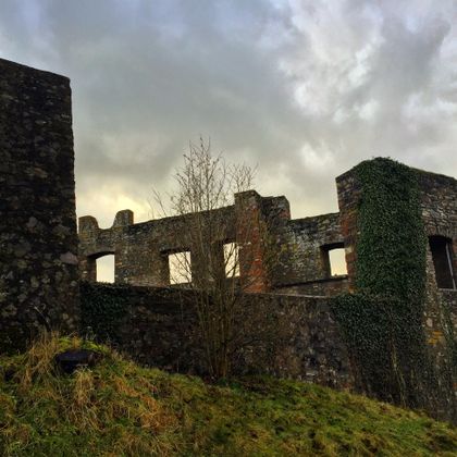 An old castle ruin with partially overgrown walls. The sky is cloudy and conveys a mystical atmosphere.
