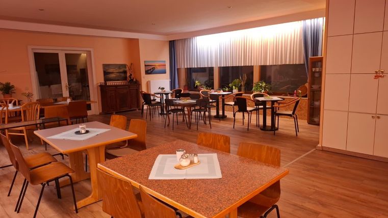 An inviting dining room with wooden chairs and tables. Large windows let in plenty of daylight and create a cozy atmosphere.