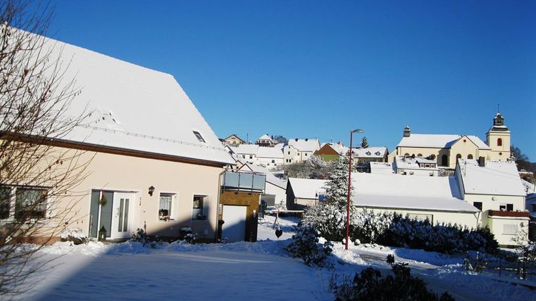 Eine verschneite Landschaft mit schönen Häusern und einem klaren blauen Himmel. Im Hintergrund ist eine Kirche zu sehen.
