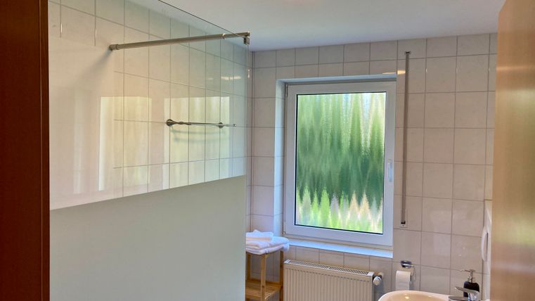 Ein modernes Badezimmer mit einer Dusche, einem Fenster und einem Waschbecken. Die Wände sind gefliest und die Einrichtung ist schlicht.