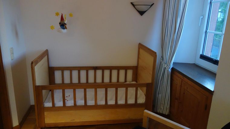 Een gezellige kinderkamer met een houten kinderbed en een raam. Er zijn lichte muren en een rustige sfeer.