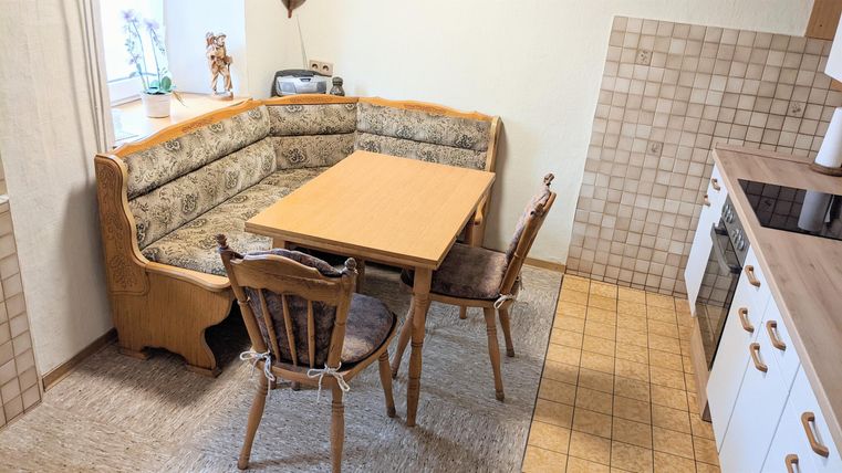 A cozy kitchen with a U-shaped seating area and a table in the center. There are wooden chairs and a bright, friendly atmosphere.