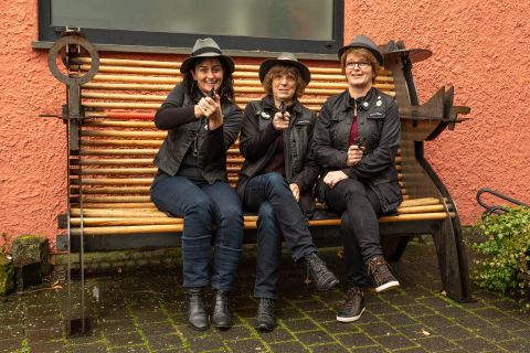 Die drei Krimiführerinnen, sitzend auf der Krimibank vor der Touristinformation Hillesheim, mit Pistolen auf den Fotografen zielend