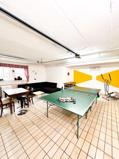 A bright room with a ping pong table and several seating options. On the wall, there are yellow accents and a window with curtains.
