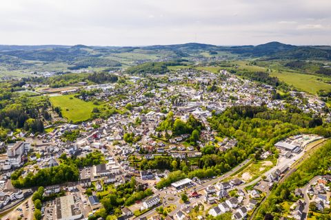 An airy view of a small town surrounded by green hills and forests. The town has numerous buildings and streets that harmoniously blend into the landscape.