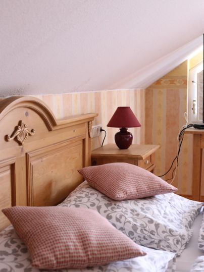 Ein gemütliches Schlafzimmer mit einem Holzbett und rosa Kissen. Neben dem Bett steht eine Lampe auf einem Nachtschrank.