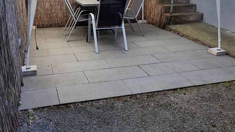 Ein kleiner Gartenbereich mit einem weißen Pavillon und einem Tisch mit Stühlen. Der Boden ist mit Platten und Kies bedeckt.