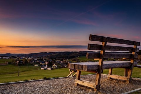 Een houten bank met uitzicht op een pittoresk landschap bij zonsondergang. Op de achtergrond zijn heuvels en een klein dorp te zien.