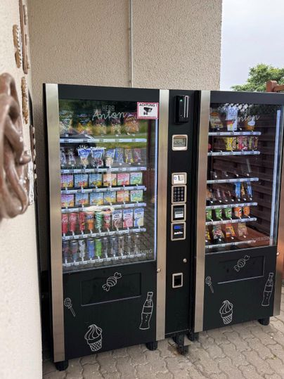 Twee drank- en snackautomaten staan naast elkaar aan een muur. Ze bieden een verscheidenheid aan snacks en verfrissingen aan.