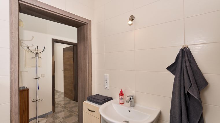 Ein modernes Badezimmer mit einem Waschbecken und Handtüchern. Die Wände sind hell gefliest und es gibt eine Tür, die zu einem anderen Raum führt.