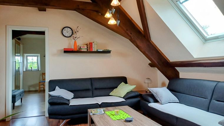 A modern living room with a high wooden ceiling and large windows. Two cozy sofas and a table create an inviting atmosphere.