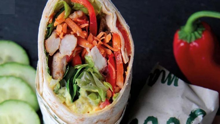 Een smakelijke wrap met kip, verse groenten en een kleurrijke vulling. Daarbij een paar komkommerschijfjes en een rode paprika.