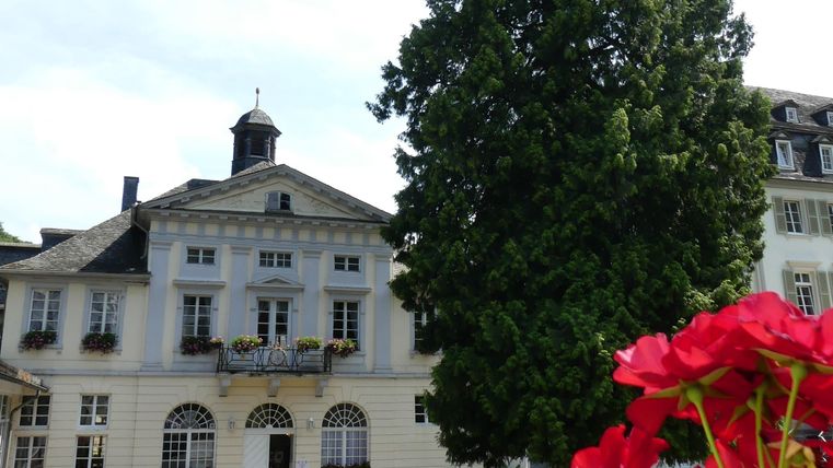 Een mooi gebouw met een hoge boom op de voorgrond. Kleurrijke bloemen sieren de scène.