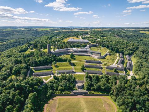 Een indrukwekkend landschap met historische gebouwen, omringd door beboste heuvels. De lucht is helder en de sfeer is vredig.