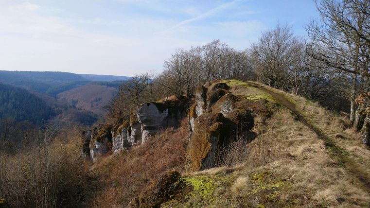 Een indrukwekkende rotsformatie met uitzicht op de groene vallei. De lucht is helder en het landschap toont een mix van beboste heuvels en open terrein.