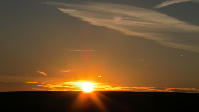 Ein schöner Sonnenuntergang am Horizont. Der Himmel ist mit sanften Wolken und warmen Farben gefüllt.