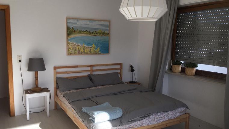 Een gezellig slaapkamer met een tweepersoonsbed en een heldere lamp. Aan de muur hangt een afbeelding van een landschap, en er staan planten op de vensterbank.