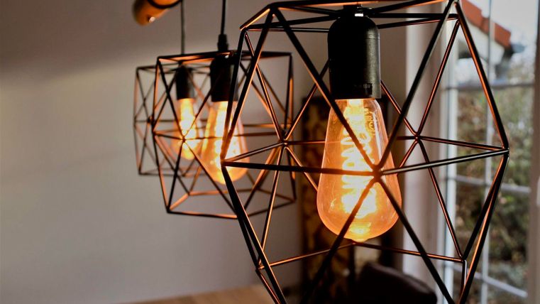 Drie geometrische lampen met warm licht hangen aan het plafond. De achtergrond is helder en huiselijk.