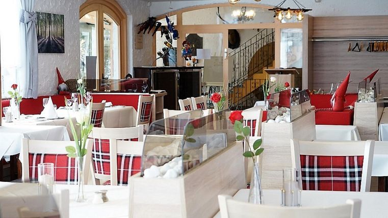 Een elegant restaurant met witte tafelkleden en rode accenten. De inrichting is modern en uitnodigend, ideaal voor een aangename maaltijd.
